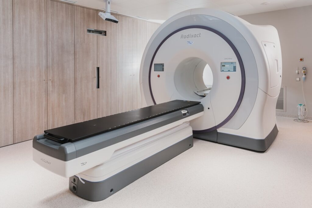 A white medical radiation therapy machine with a black patient table in a clinic
