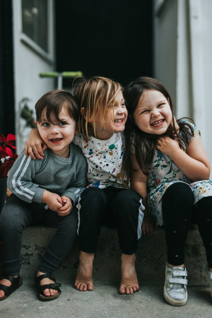 Three children sitting together on concrete steps, laughing and hugging