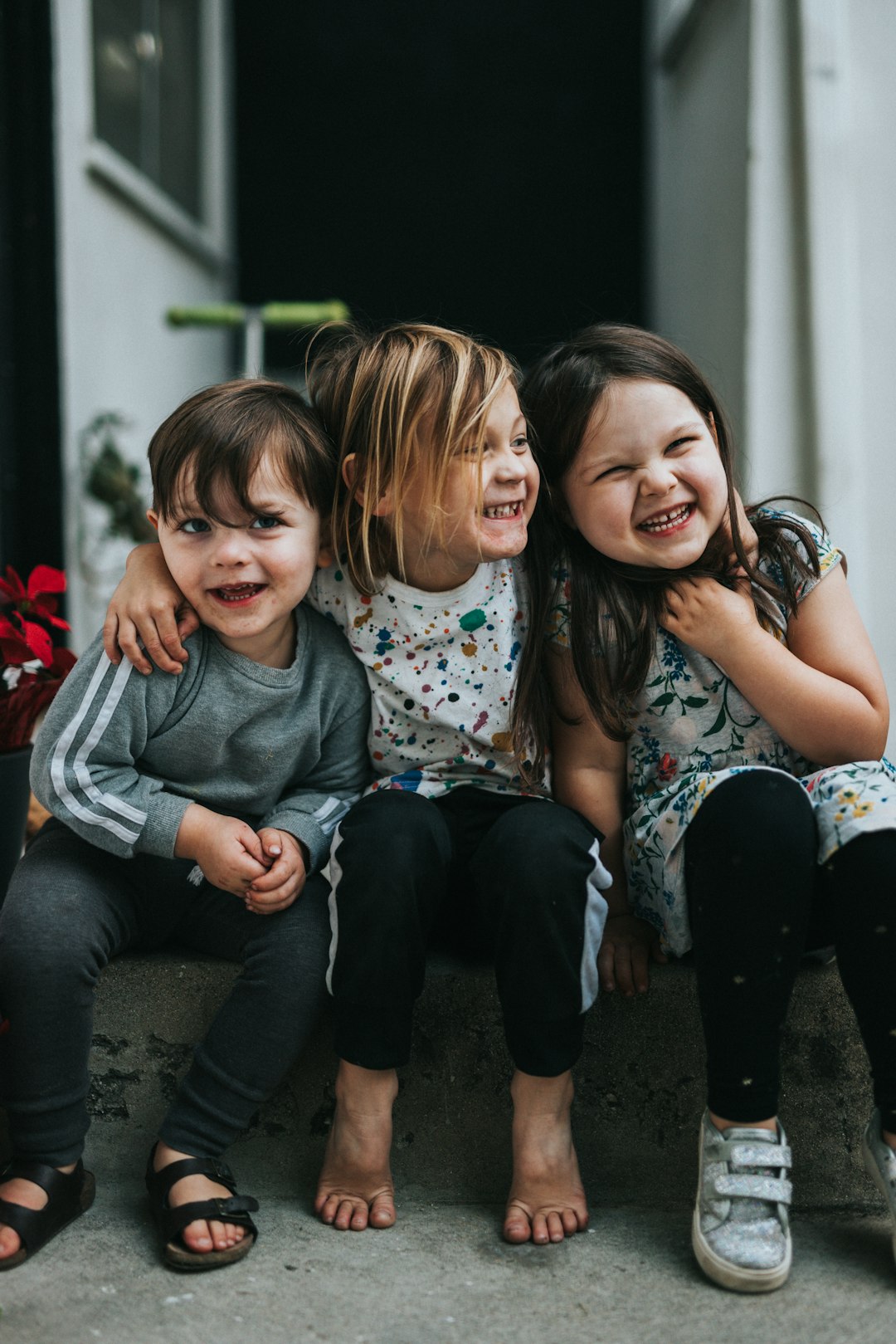 Three children sitting together on concrete steps, laughing and hugging